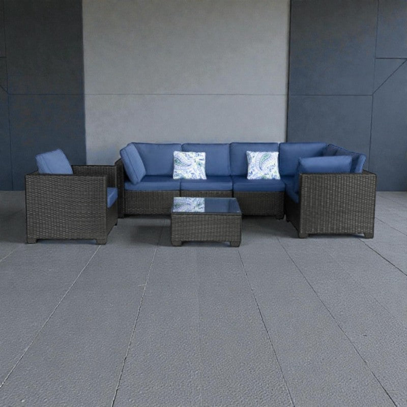 Coocosh Rattan Sectional Sofa with blue cushions and decorative pillows, perfect for outdoor relaxation and entertaining guests. This versatile furniture set is positioned on a gray patio, showcasing its spacious L-shaped configuration and accompanying co