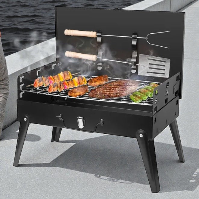 Coocosh portable charcoal grill in black, cooking skewers, steaks, and vegetables on a grate with smoke rising, featuring a hinged lid and a utensil holder for outdoor grilling enjoyment.