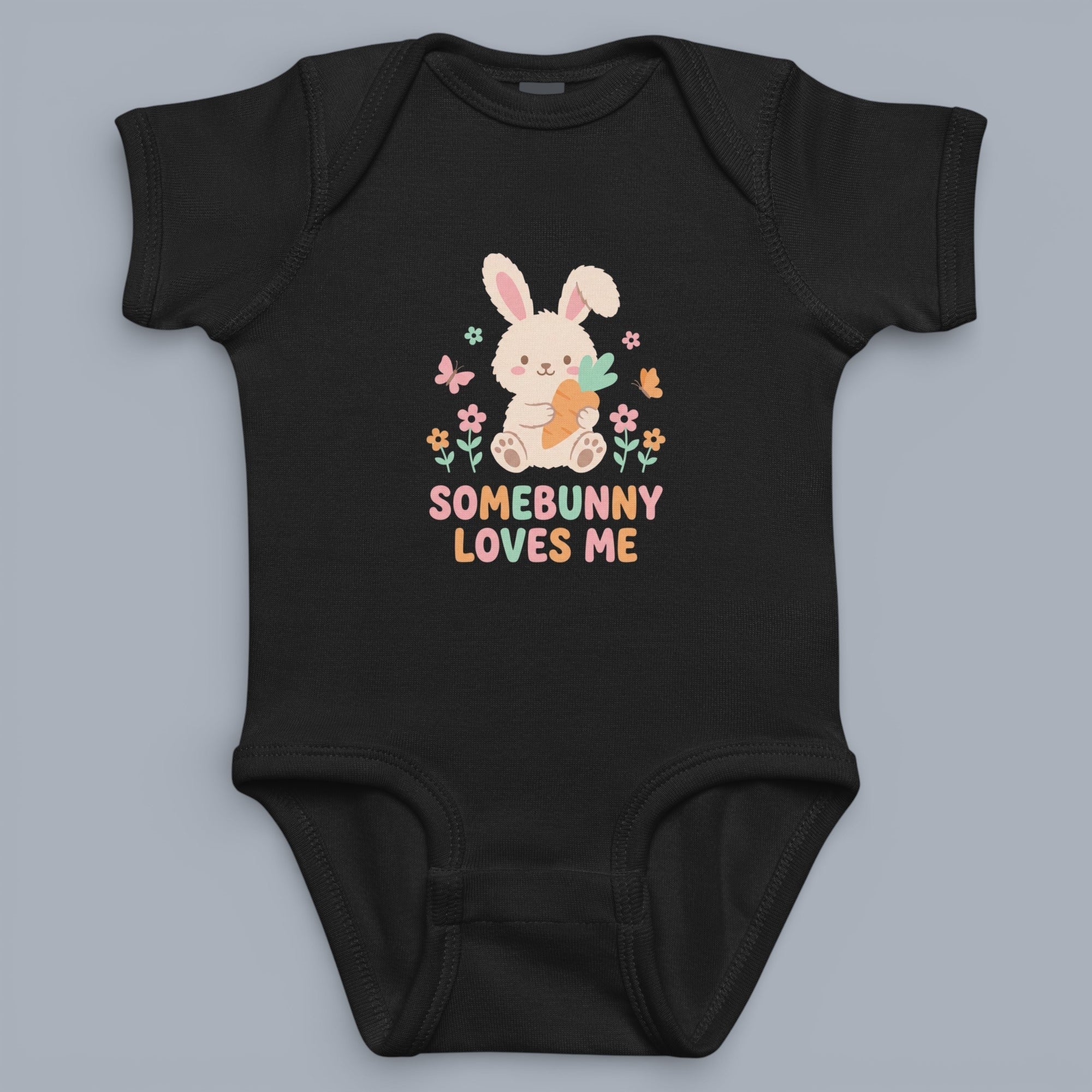Coocosh baby bodysuit featuring a cute bunny holding a carrot, surrounded by flowers and butterflies. The text "Somebunny Loves Me" adds a touch of warmth. Made of soft, black cotton, ideal for infants. This onesie is perfect for Easter or everyday wear. 