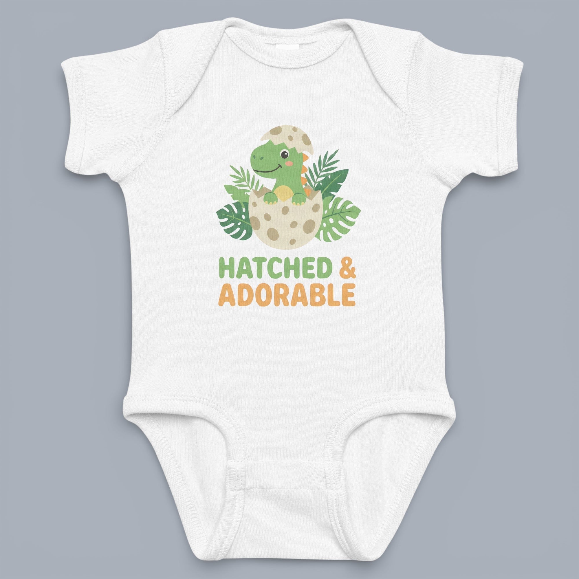 Coocosh Baby Onesie featuring a cute dinosaur hatching from an egg design and "Hatched & Adorable" text printed on the front, made from soft, white cotton in a close-up product shot.