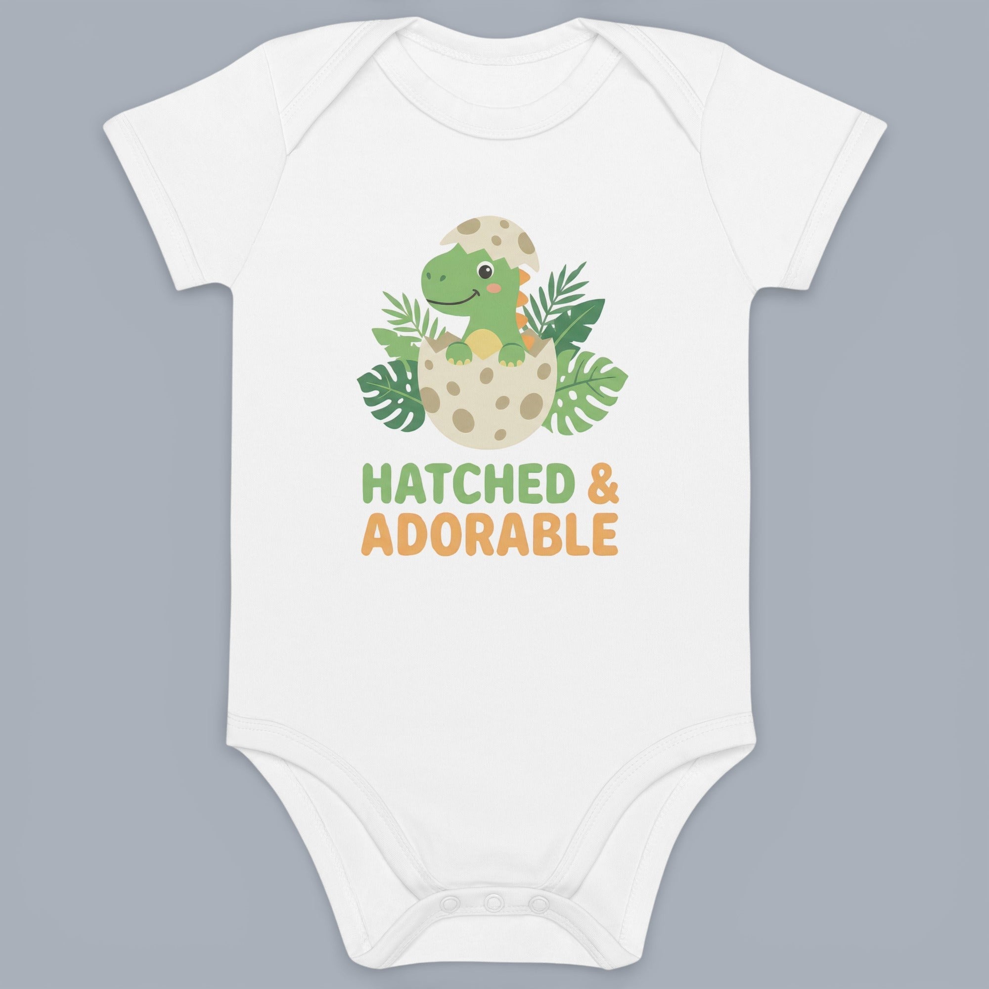 Coocosh Baby Onesie features a cute dinosaur hatching from an egg with "Hatched & Adorable" text, made of soft, breathable fabric. The white onesie offers comfort and style for infants and toddlers. A charming outfit for your little one.