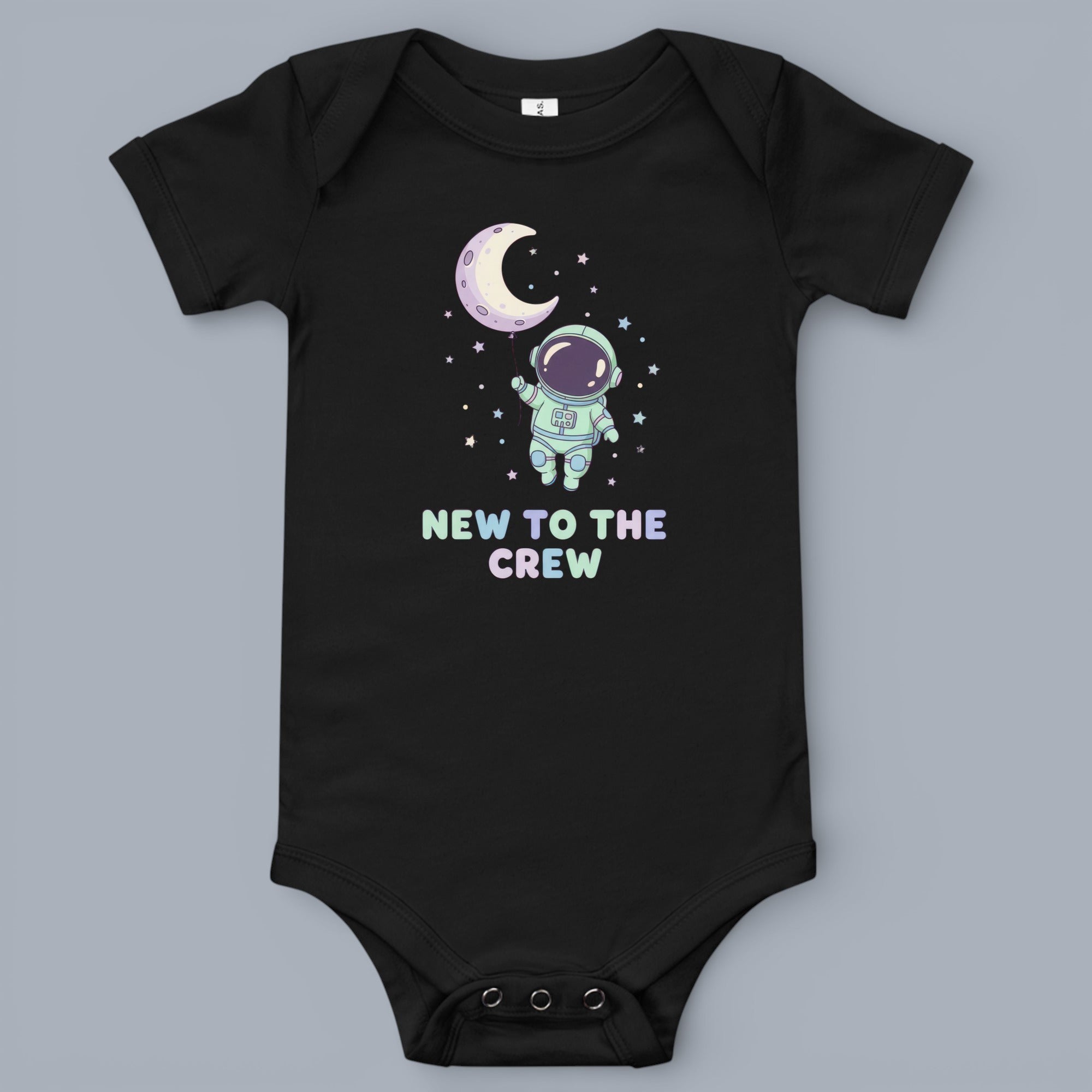 Coocosh Baby Onesie featuring an astronaut holding a moon balloon graphic, surrounded by stars, with the text 'New to the Crew' printed on black cotton fabric. A sweet addition for baby's space themed wardrobe period.