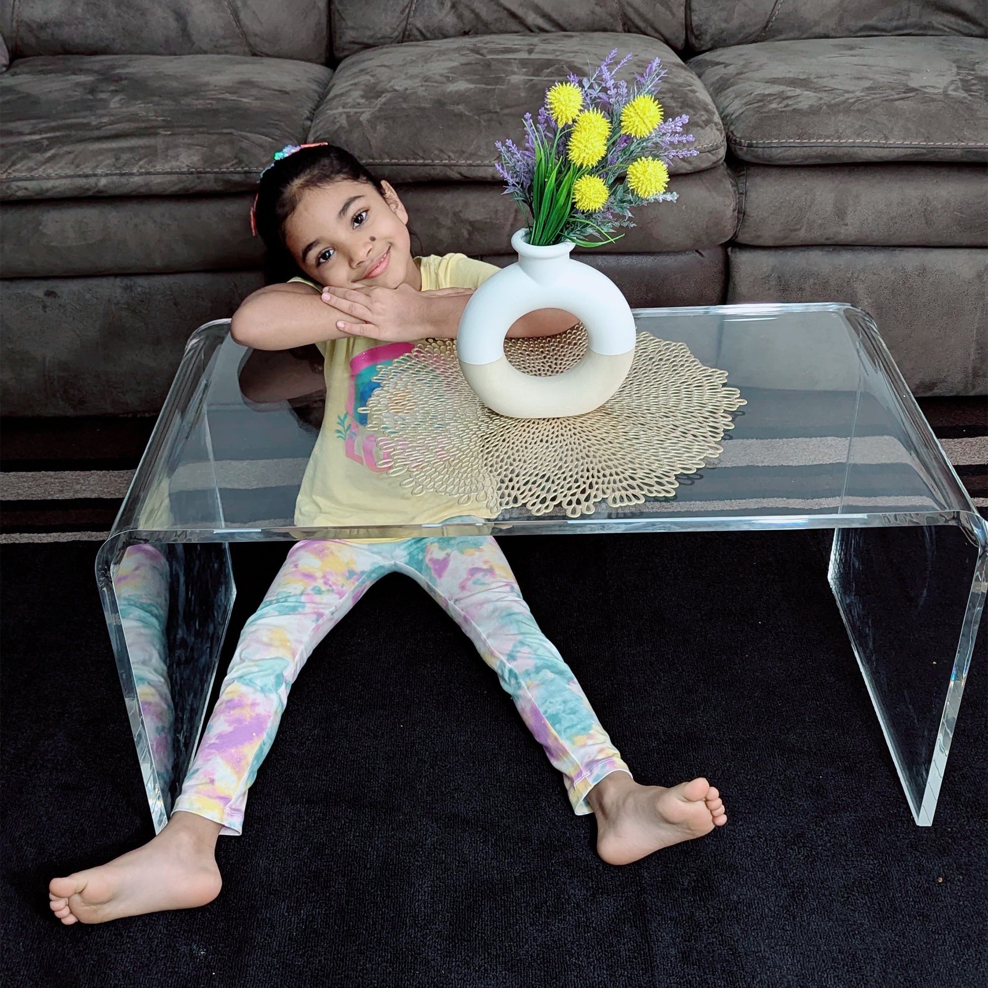 Clear Acrylic Coffee Table with Unique Design, featuring a playful child in colorful tie-dye leggings sitting beneath it, creating a fun and inviting living room atmosphere.