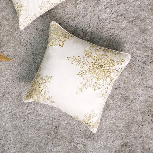Coocosh white square throw pillow with gold embroidered snowflake details, showcasing intricate stitching and a sparkling center jewel on a soft gray shag rug. This decorative pillow adds a touch of winter elegance to any cozy space, presented in a close-