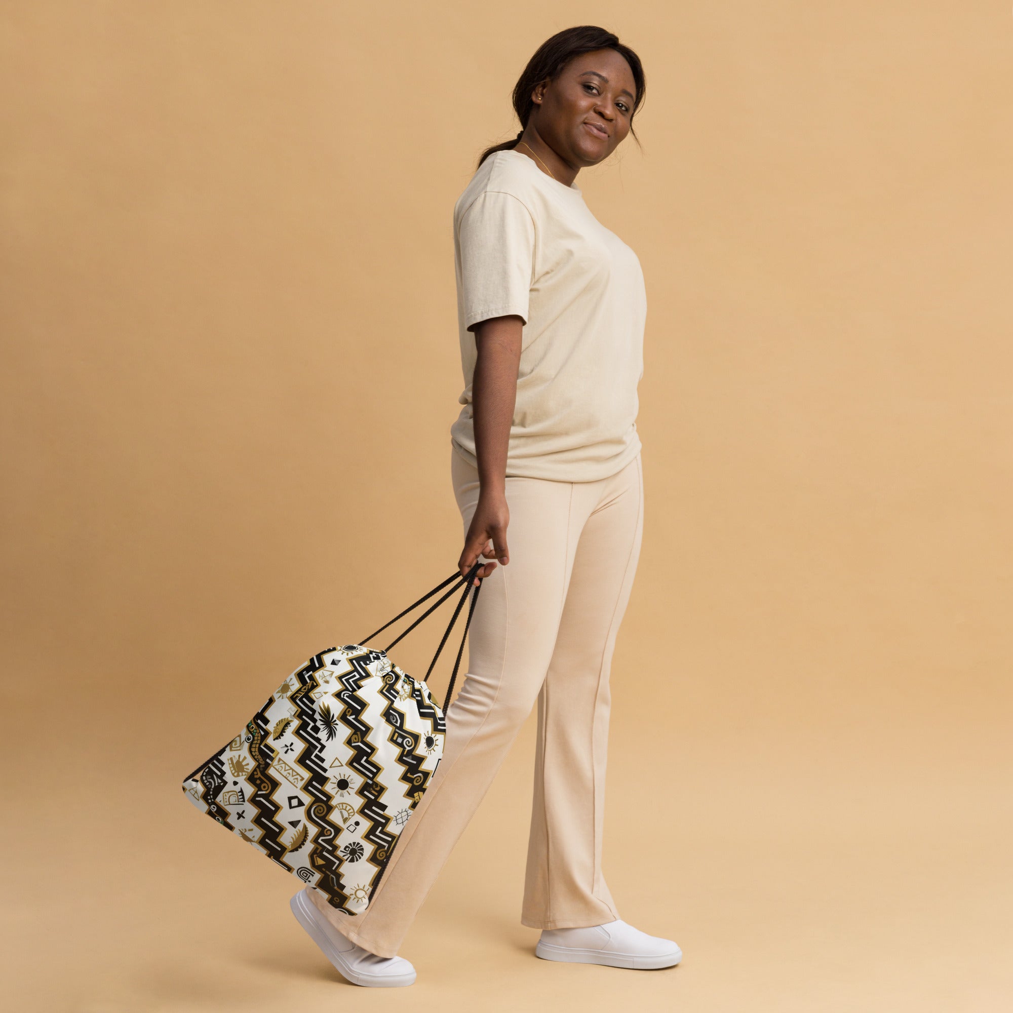 Coocosh Serpents Path drawstring bag, showcasing geometric snake patterns in a relaxed, light outfit setting. This durable 100% polyester accessory promises easy access and effortless style, perfect for gym sessions or everyday errands.