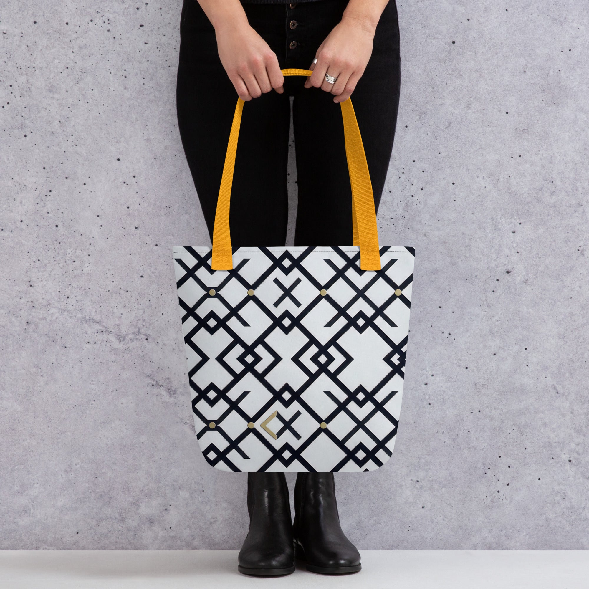 Coocosh Midnight Meridian tote bag, featuring a chic geometric black and white pattern with vibrant yellow straps, offers a spacious and durable accessory for stylish outings, combining fashion and functionality against a soft gray backdrop.
