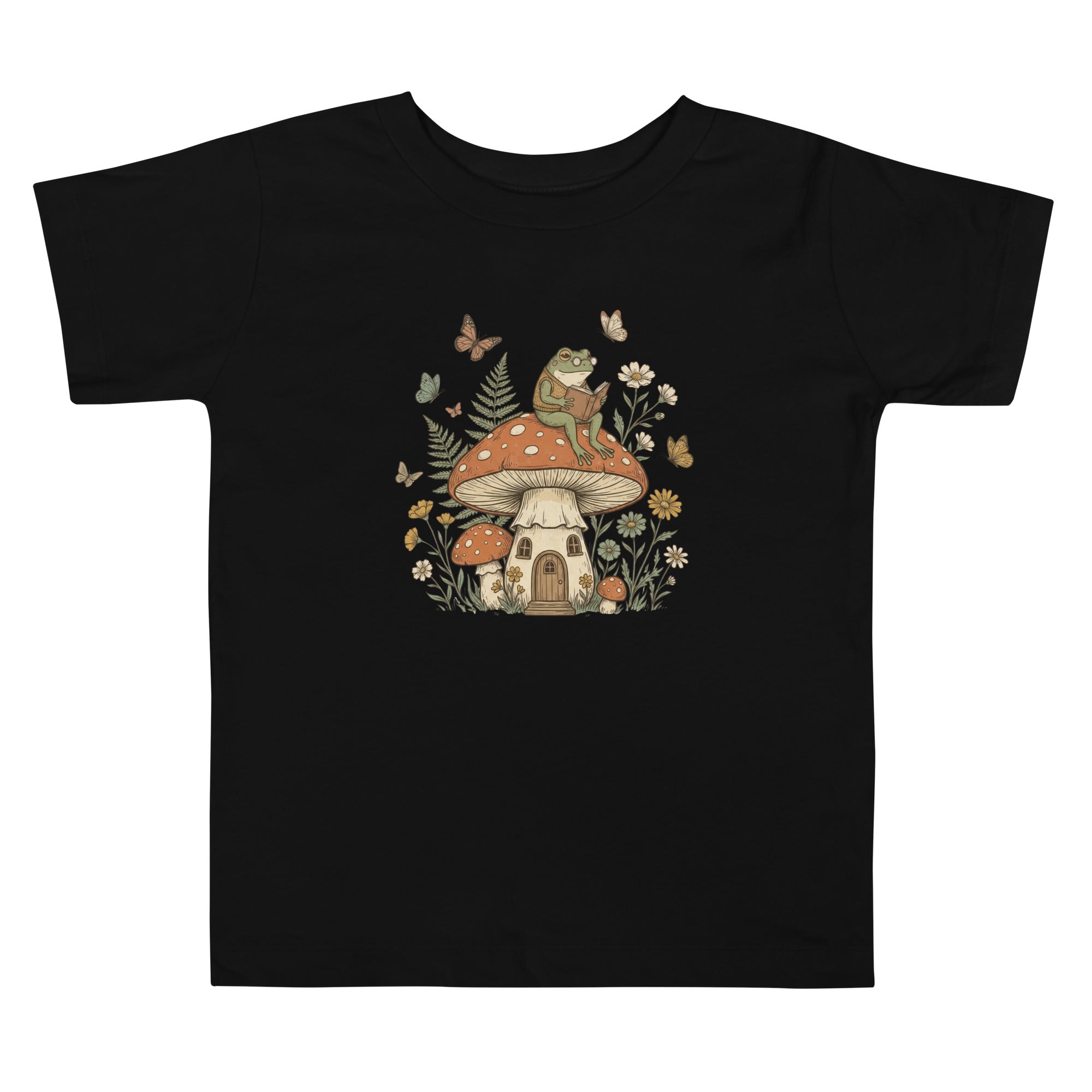 Coocosh t-shirt featuring a whimsical frog reading a book atop a mushroom house surrounded by butterflies and flowers. This charming black tee is perfect for nature lovers. Great design.